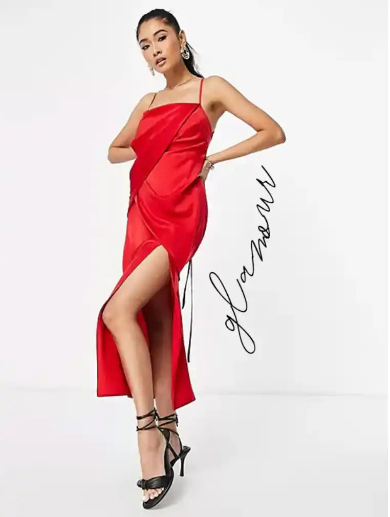 Une femme en robe nuisette en satin rouge avec une fente latérale et des talons hauts noirs à brides.