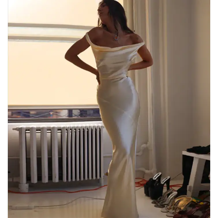 Femme élégante portant une robe longue dos nu en satin, style sirène, sans manches, en coton-lin, idéale pour les soirées et événements chic. Couleur beige.