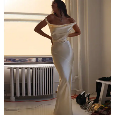 Femme élégante portant une robe longue dos nu en satin, style sirène, sans manches, en coton-lin, idéale pour les soirées et événements chic. Couleur beige.