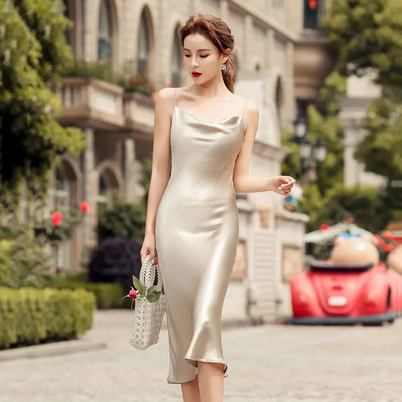 Robe longue satinée dos nu couleur champagne, fluide et élégante, inspirée du style vintage français, portée lors d’un événement en extérieur.